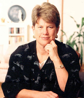 Ann Markusen sitting and smiling, resting her chin against one hand. 