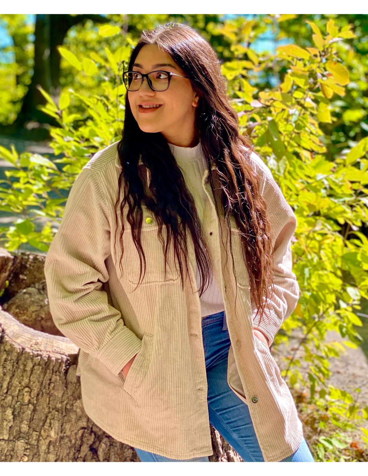 Nida sits on a tree stump and looks over her right shoulder 