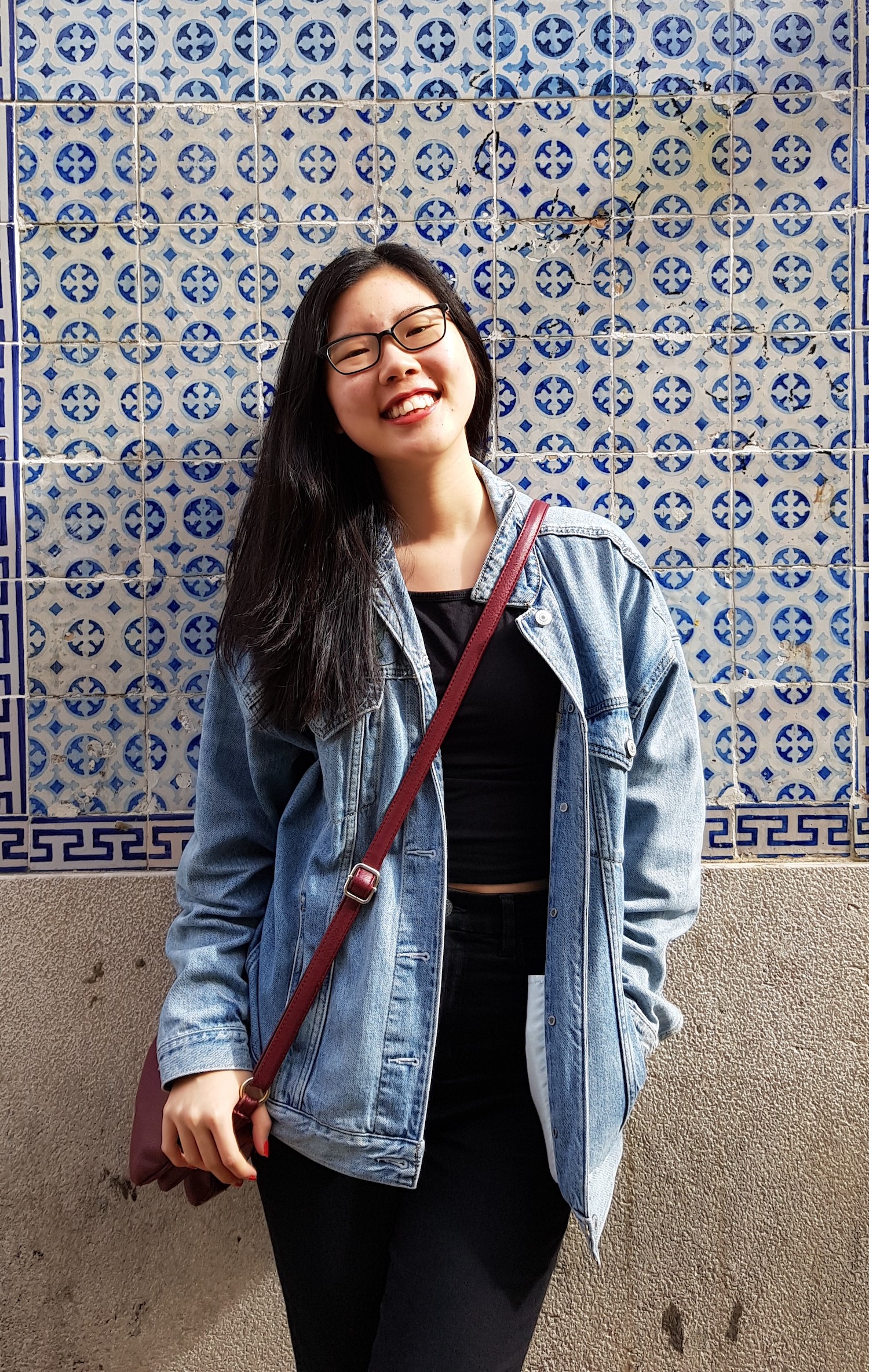 Michelle standing and smiling in front of a tiled wall.